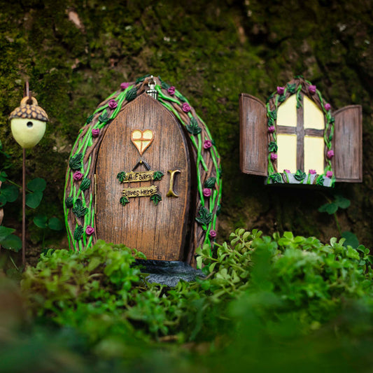 Hand-painted opening fairy door and window set mounted on a tree trunk showing glow in the dark windows at dusk